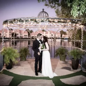 Couple embracing under a beautifully decorated gazebo at Swan Garden, Las Vegas, with a serene lake backdrop, ideal for romantic wedding ceremonies.