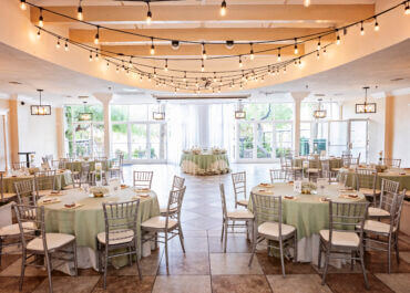Elegant reception hall setup with round tables, green linens, and string lights, showcasing a beautifully designed space for all-inclusive Las Vegas wedding celebrations.