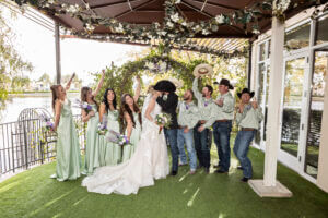 Bride and groom celebrating with wedding party in green attire under floral gazebo at Lakeside Weddings & Events venue in Las Vegas.